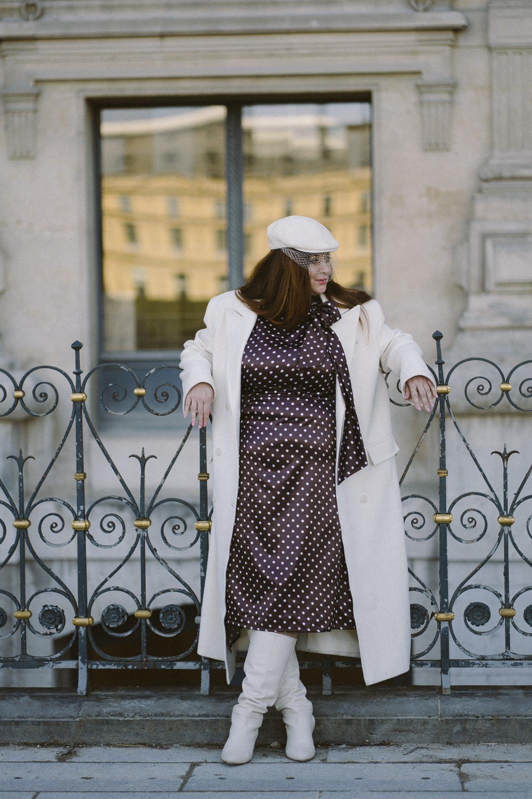 Oksana Katerynych, robe à pois, foulard, devant une grille en fer forgé